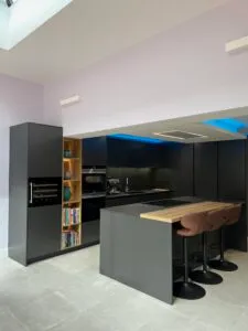 Loughton kitchen with Caneo dark graphite cabinetry, natural oak island and open illuminated shelving