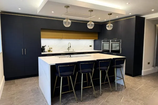 Elegant navy blue kitchen in Harpenden featuring quartz worktops, a waterfall island and integrated NEFF appliances
