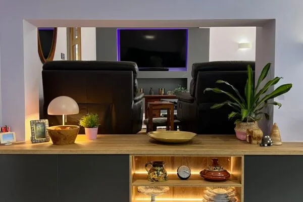 Dark grey kitchen with natural oak worktop and illuminated open shelving leading into the living area